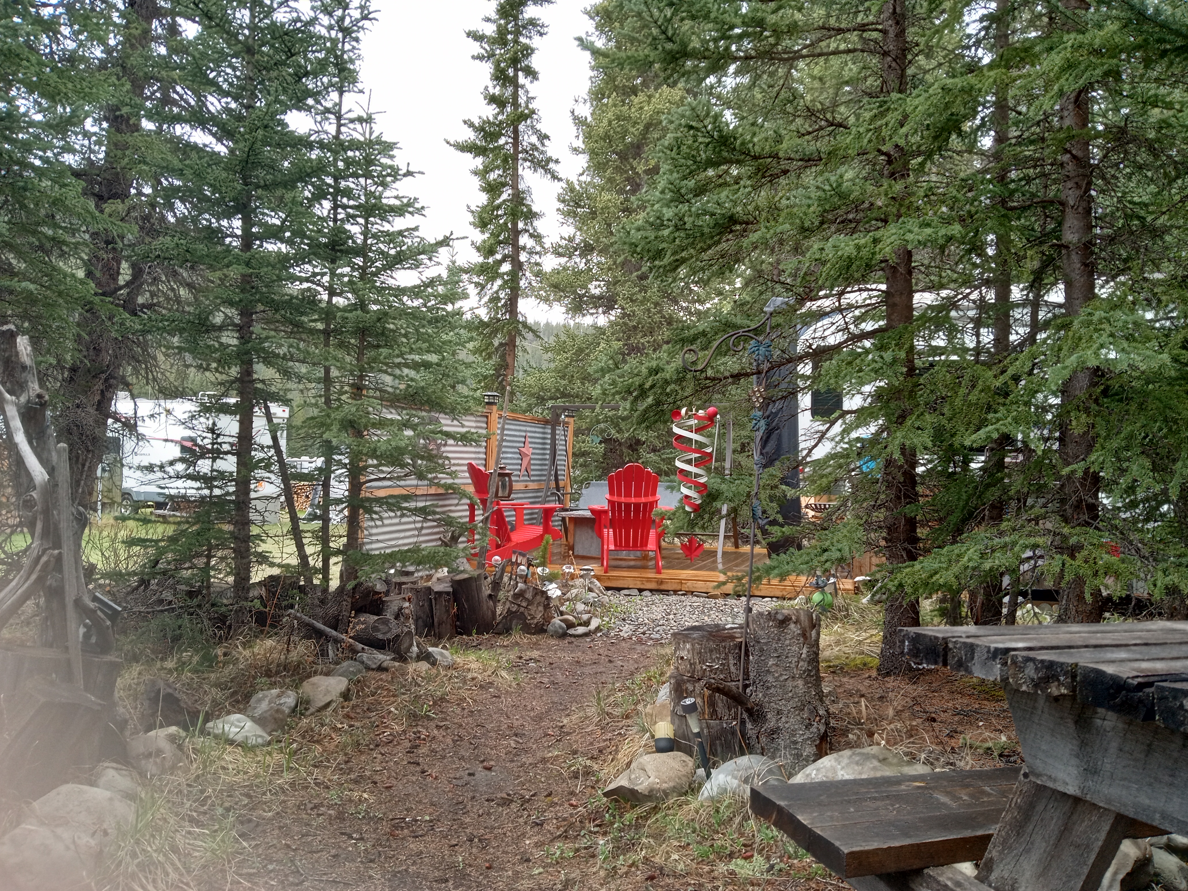 Treed RV site with red Adirondack chairs and deck — Barrier Mountain Outfitters